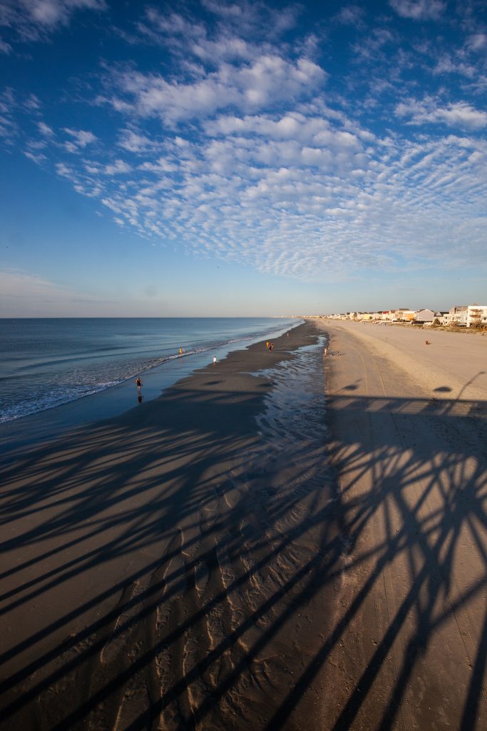 Shadows cast by a pier in the early morning stretch down Surfside beach in South Carolina